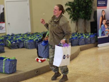 Service member carrying two bags full of food at a Holiday Meals for Military event.