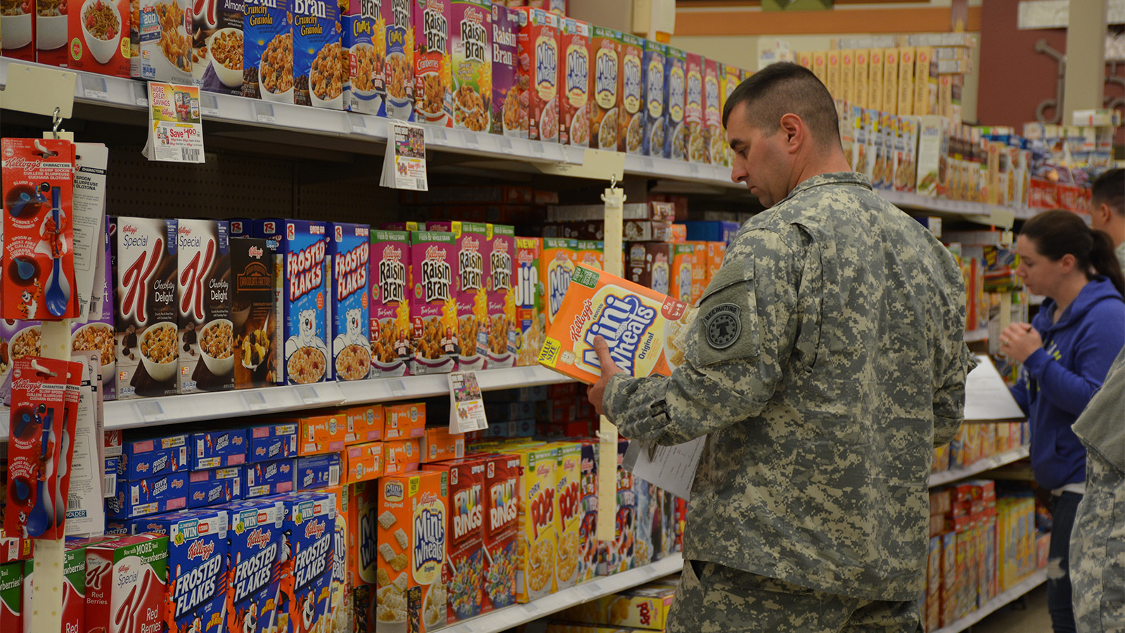 Service member holding a box of cereal in a grocery store.