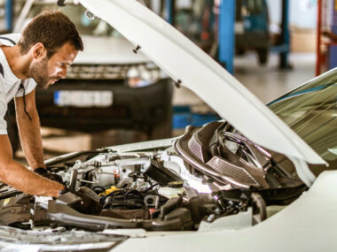 Man working under the hood of a white vehicle.