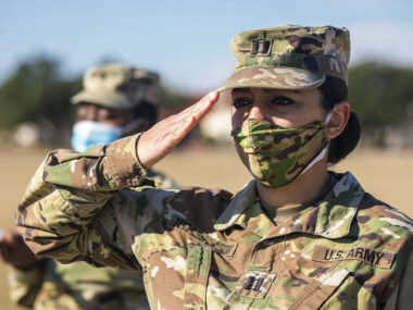 Female Army Soldier saluting outdoors and with a mask on.