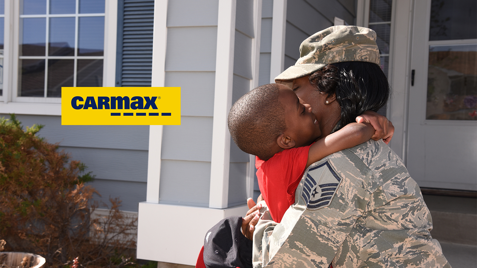 Female service member hugging her son in front of a house.