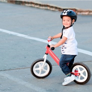 Small child riding bike with a helmet on outside.