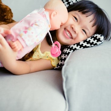Young girl is laying on a couch and holding a baby doll.