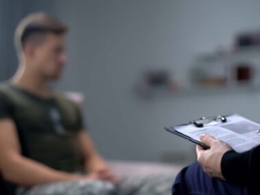 Service member sits on couch while a counselor takes notes. The counselor is sitting across from the service member.