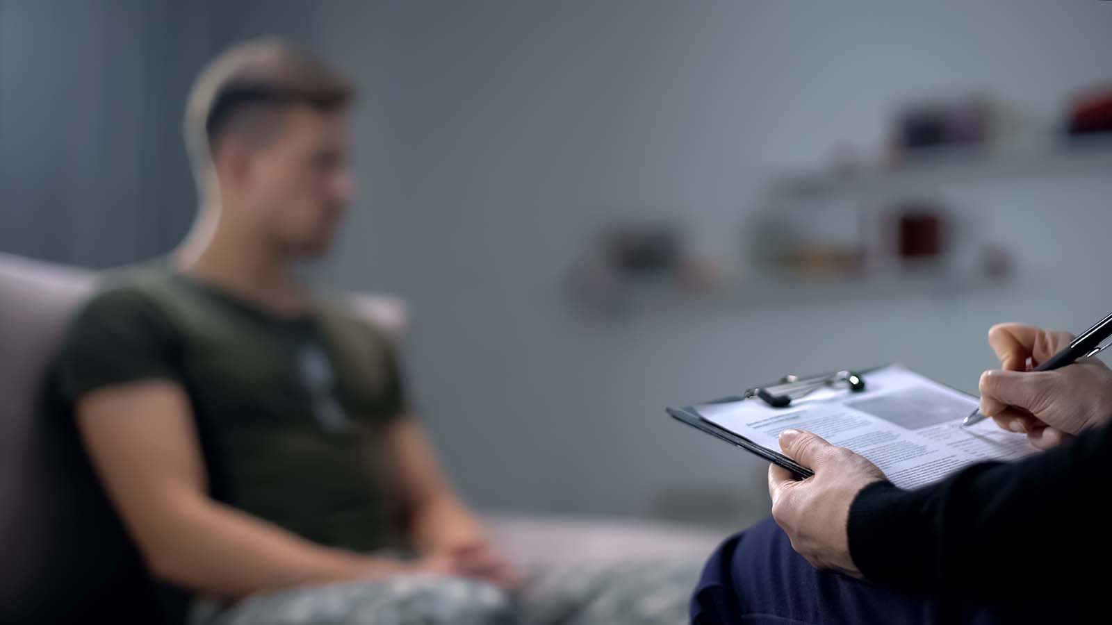 Service member sits on couch while a counselor takes notes. The counselor is sitting across from the service member.