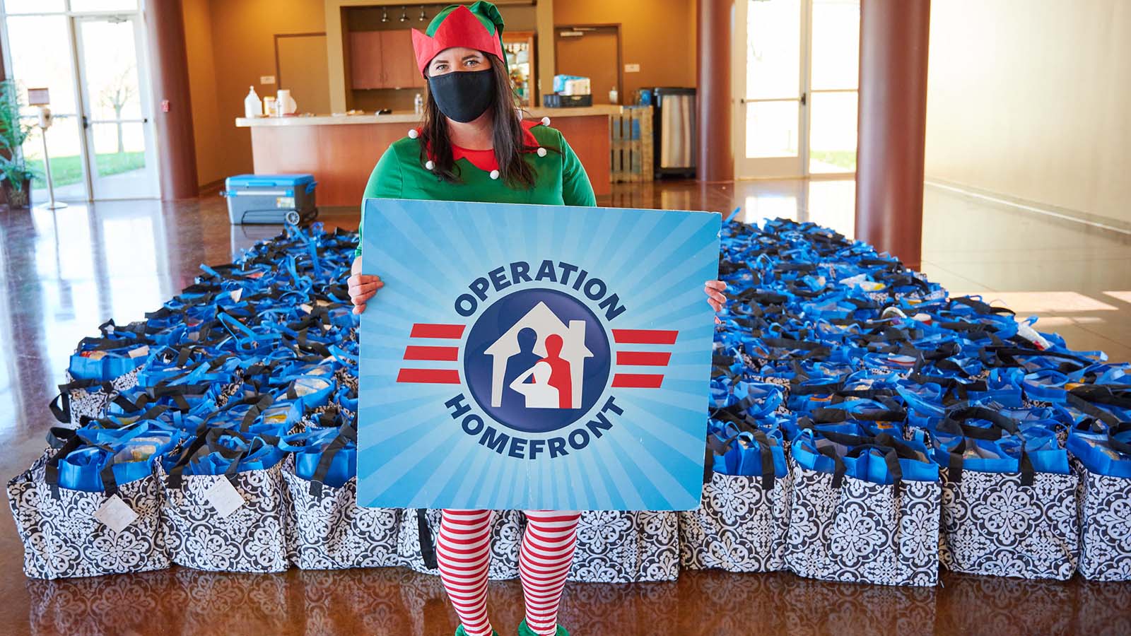 Operation Homefront volunteer dressed as an elf holding a sign at a Holiday Meals for Military event.