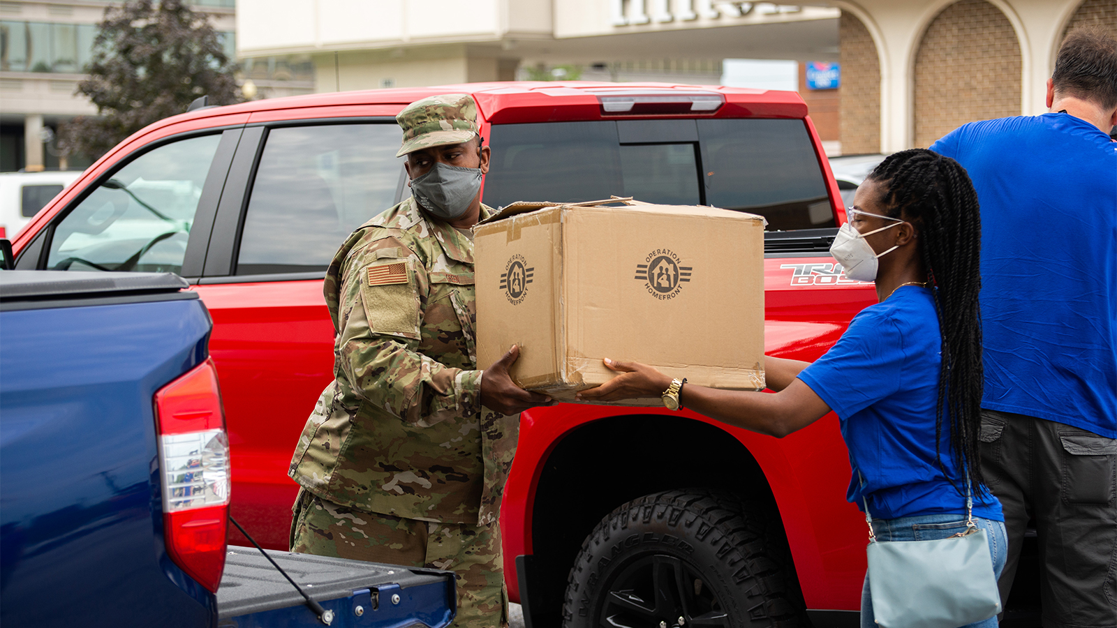 Service member is receiving a large box from a volunteer at an event.
