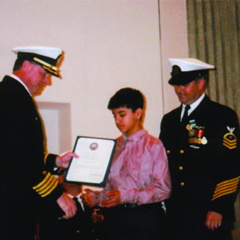 Military personnel giving an award to young boy.