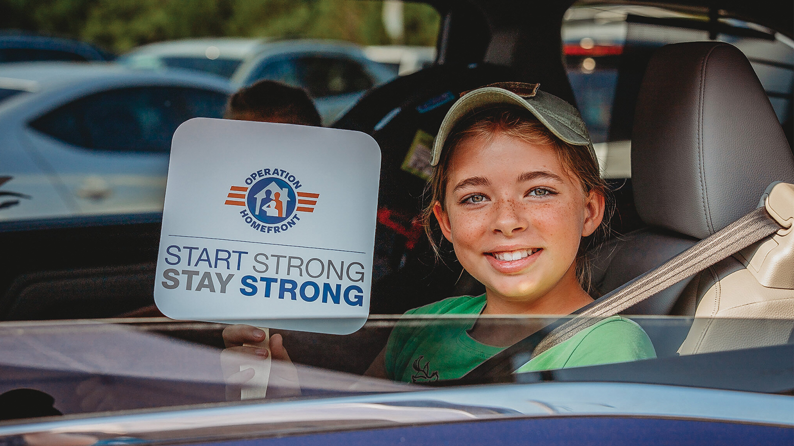 Child pictured in a car window holding a sign.