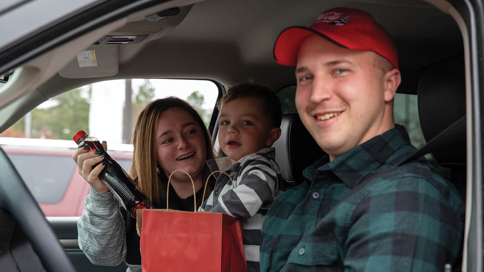 A family smiling in a car as they receive holiday meals.