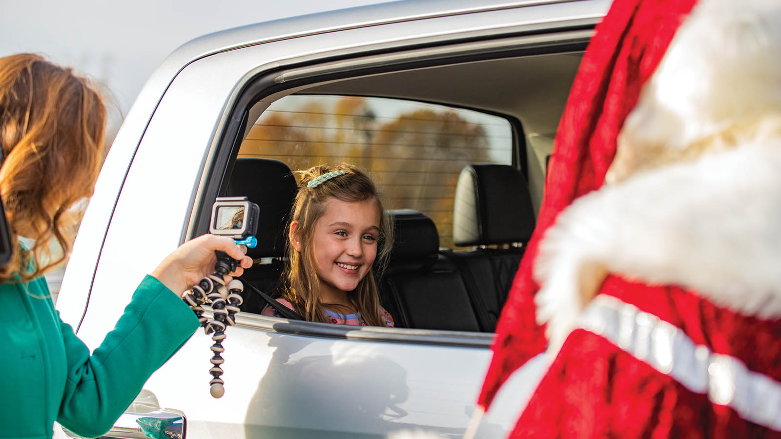 A little child smiling at Santa who is standing outside of the car.