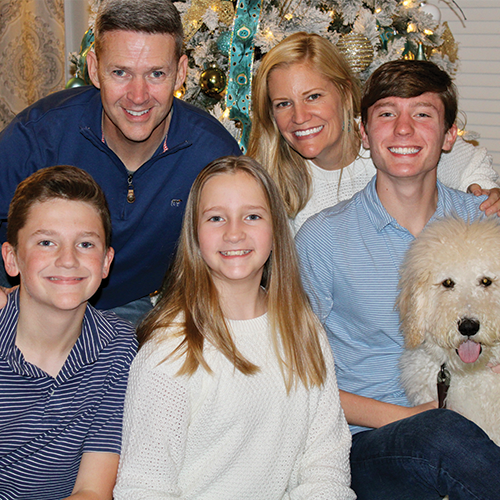 family and dog smiling in front of Christmas tree